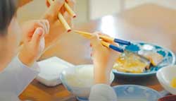 映画の一場面。親が子どもに箸の持ち方を教えて褒めているシーン