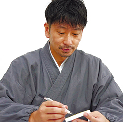 作務衣（さむえ）を着用し、仏教モチーフの消しゴムはんこを制作中の筆者